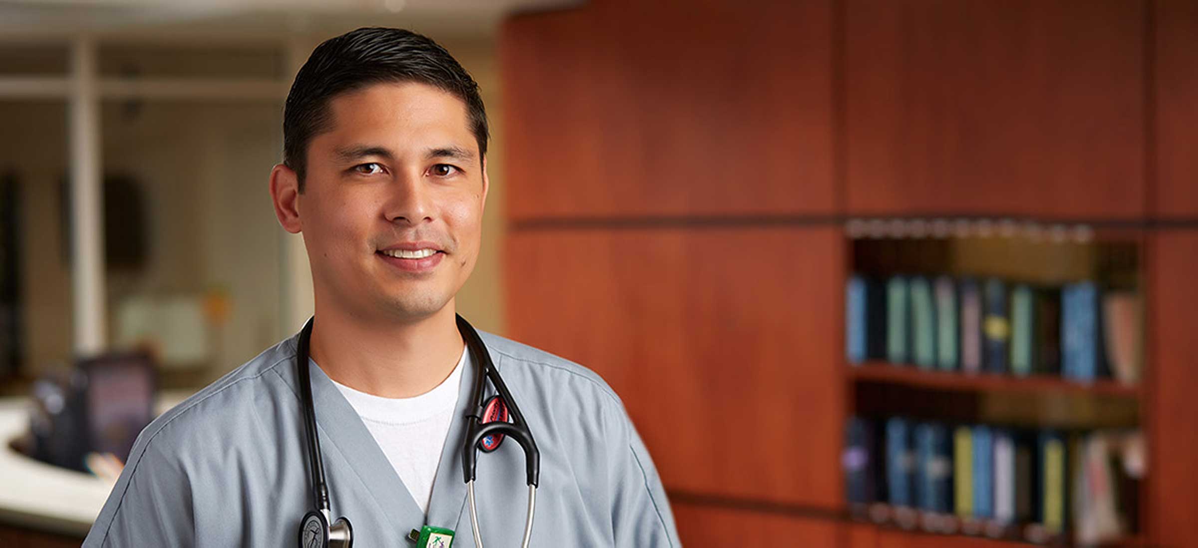 A smiling nurse wearing scrubs and a stethoscope.