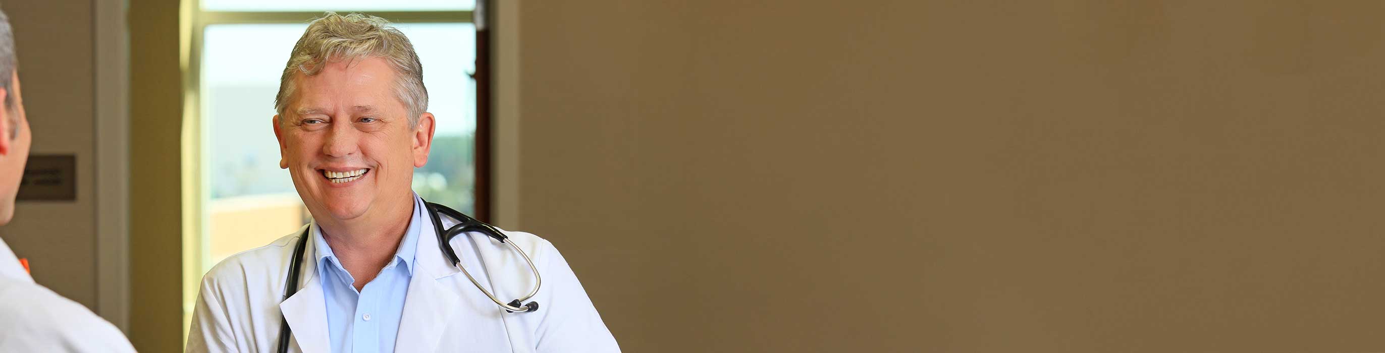 A smiling physician wearing a white lab coat and a stethoscope.